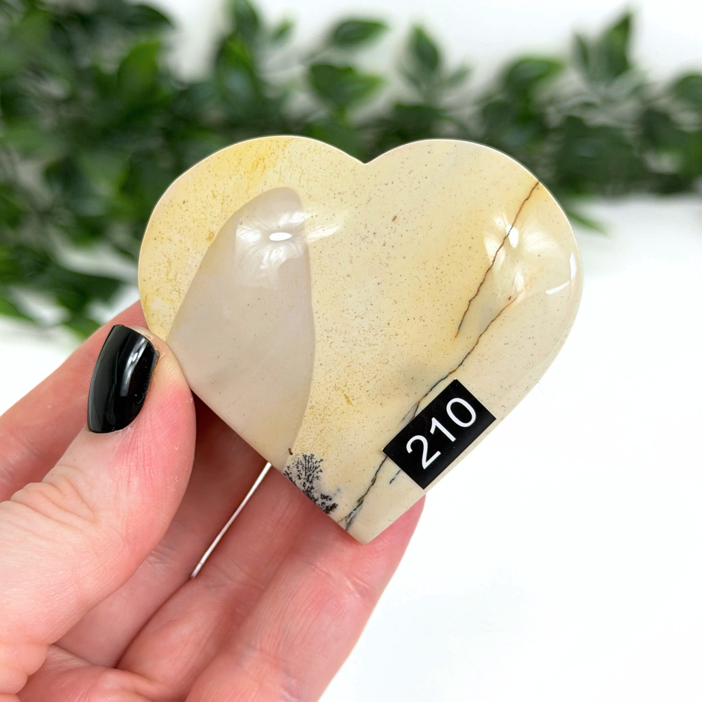 Heart-shaped mookaite stone held in a hand with a blurred green background