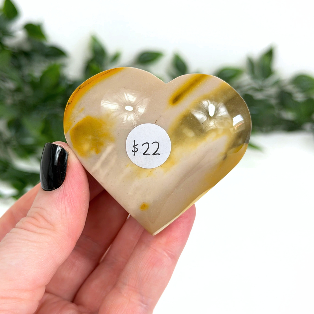 Heart-shaped mookaite stone with a price tag held by a hand against a blurred green background