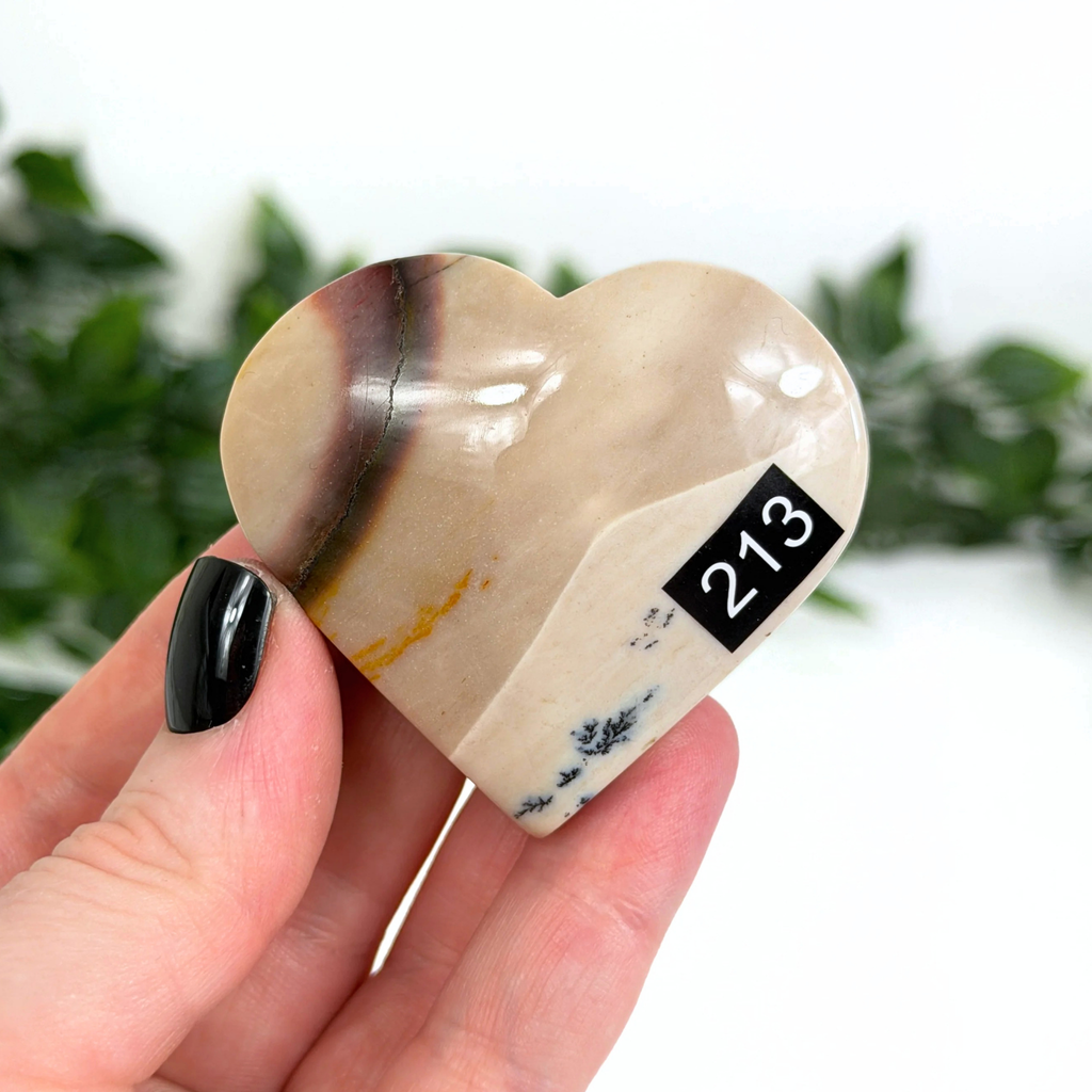 Heart-shaped mookaite crystal with '213' marking held in a hand against a blurred green background