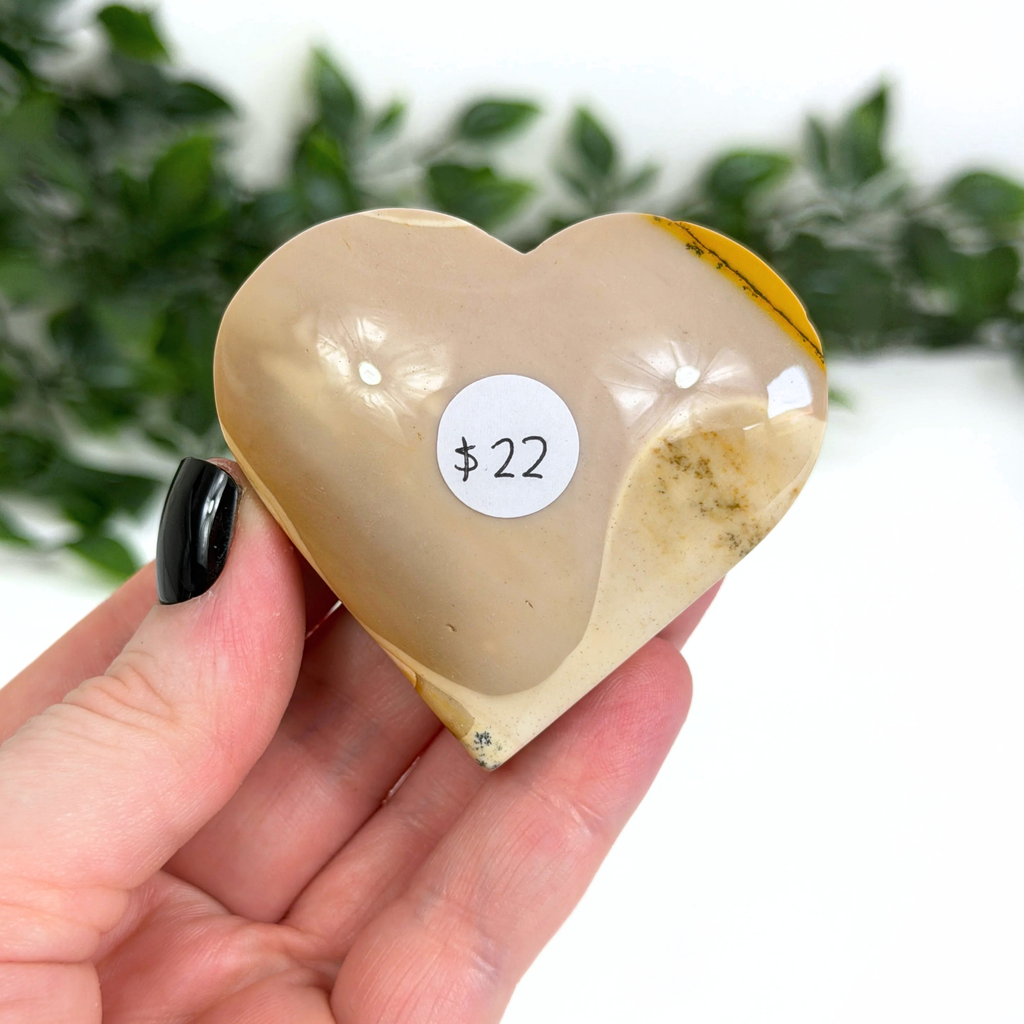 Heart-shaped mookaite crystal with a price tag held in a hand against a blurred green background