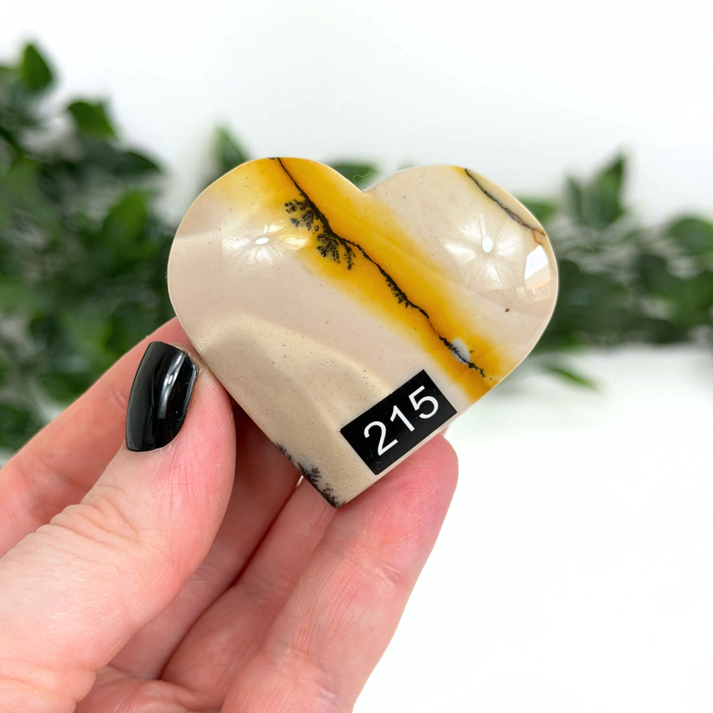 Heart-shaped mookaite stone held in a hand with a blurred green background