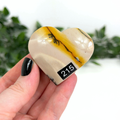 Heart-shaped mookaite stone held in a hand with a blurred green background