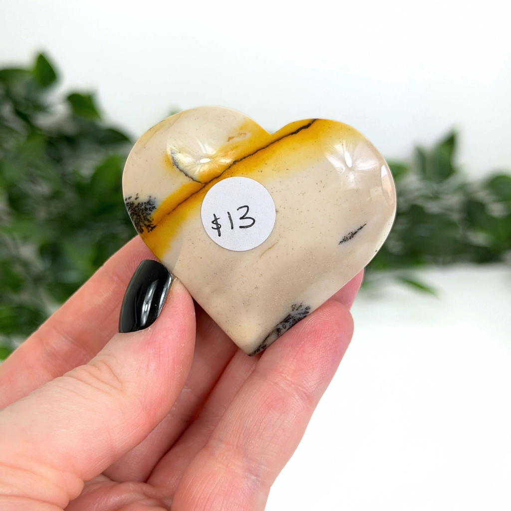 Heart-shaped mookaite crystal held in a hand with a price tag sticker, greenery in the background