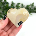 Heart-shaped mookaite stone held in a hand with a blurred green leafy background