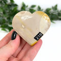 Heart-shaped mookaite crystal held in a hand with a blurred green leafy background