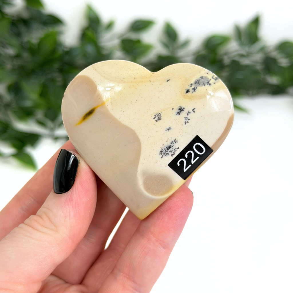 Heart-shaped mookaite with a label on a hand against a blurred green background